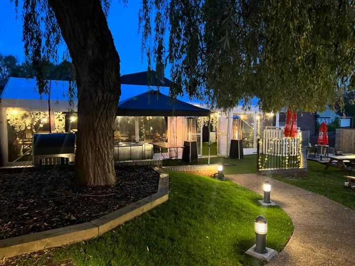 pathway illuminated leading to a marquee with a large hanging tree