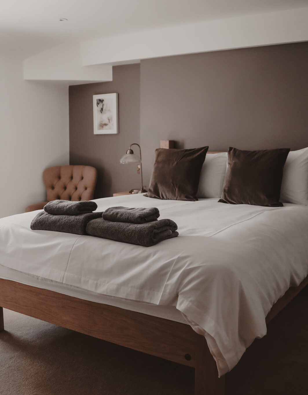 bed against a brown wall with pillows and towels on the foot of the bed