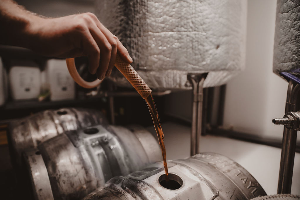 Pipe pouring beer into a grey barrel in a cellar